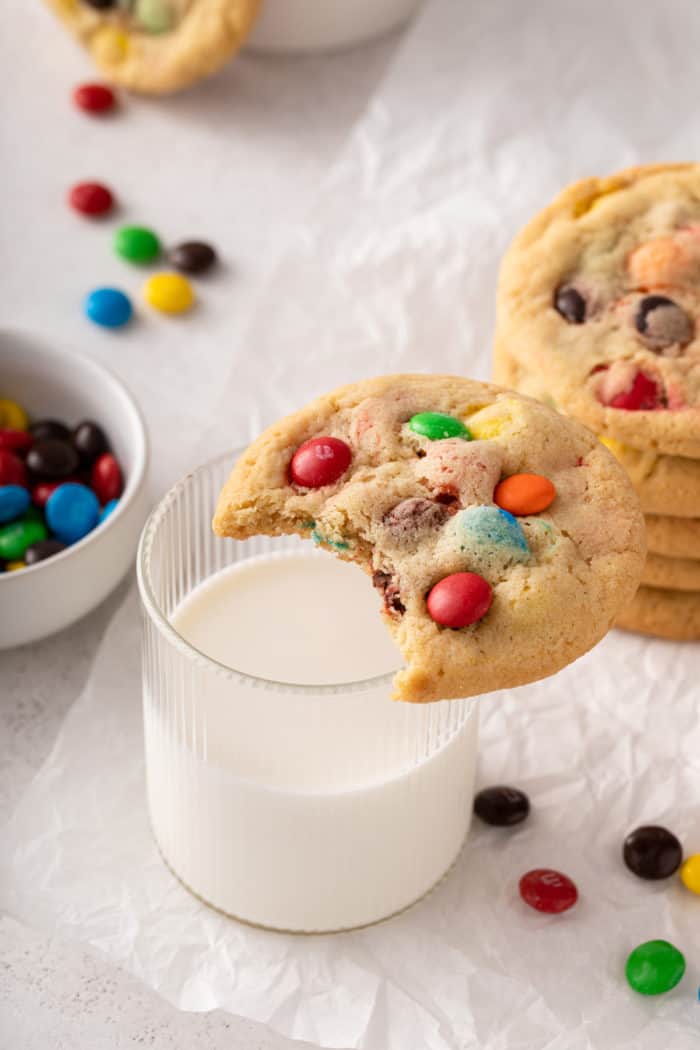 M&M cookie with a bite taken out of it set on the edge of a glass of milk.