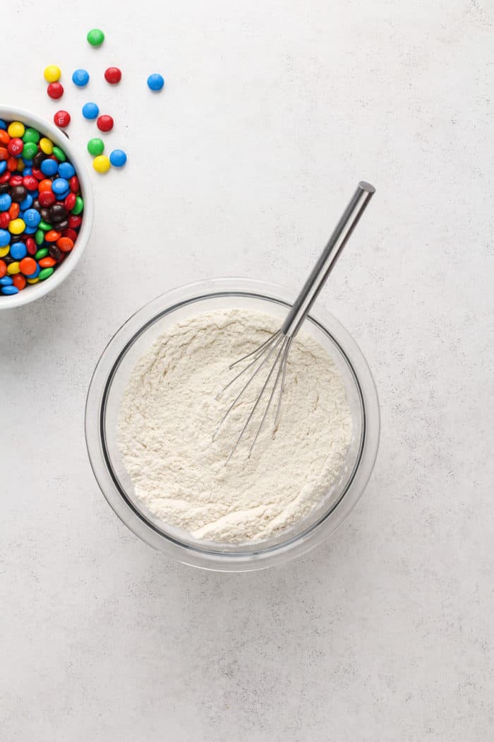 Dry ingredients for M&M cookies being whisked together in a glass bowl.