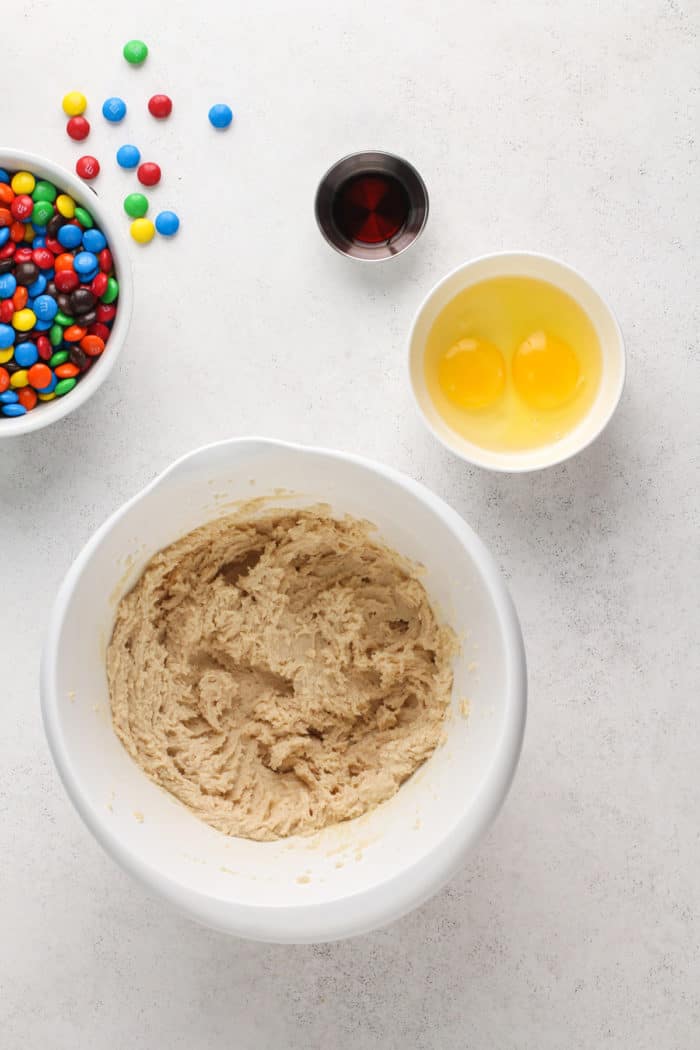 Butter and sugar creamed together in a white bowl, set next to smaller bowls of eggs and vanilla.