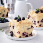 Slice of blueberry coffee cake on a white plate, with additional plated slices in the background.