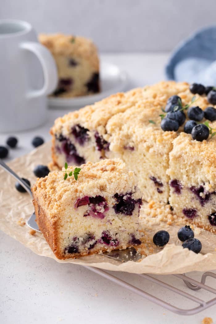 Plated slices of blueberry coffee cake on a countertop next to coffee creamer and a bowl of blueberries.