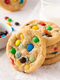 Stack of 4 m&m cookies on a piece of parchment paper with another cookie leaning against the stack.
