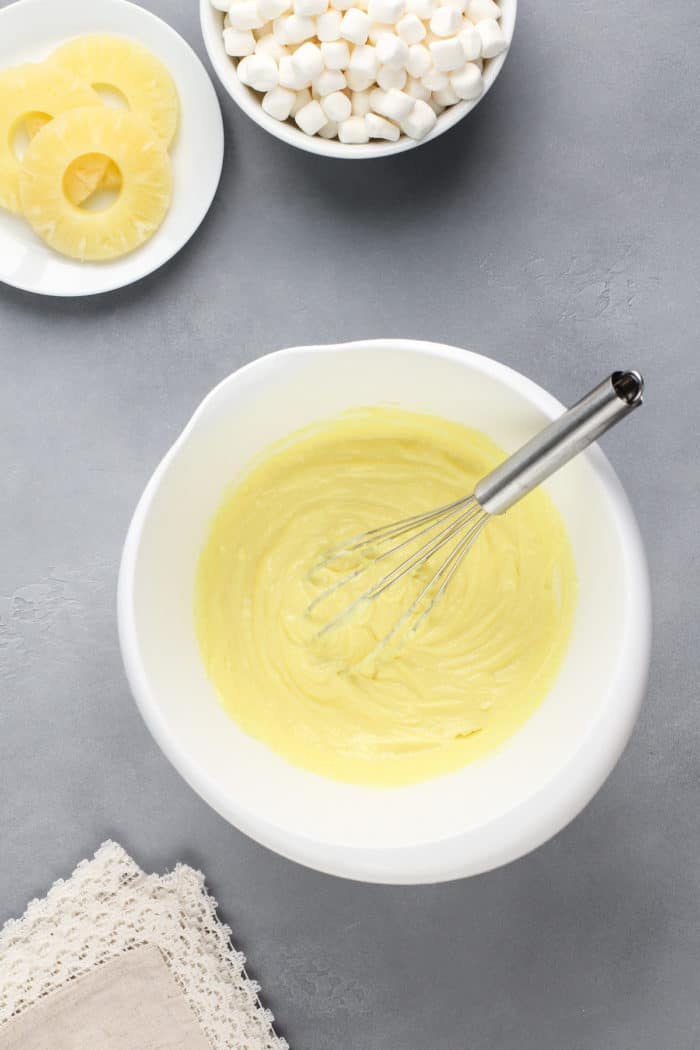 Pureed cottage cheese and pineapple jello whisked together in a white mixing bowl.