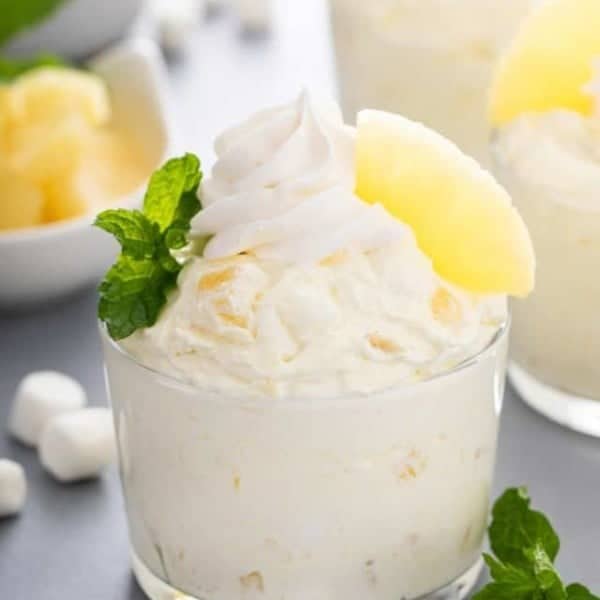 Closeup image of a glass cup filled with pineapple fluff and topped with whipped topping and pineapple.