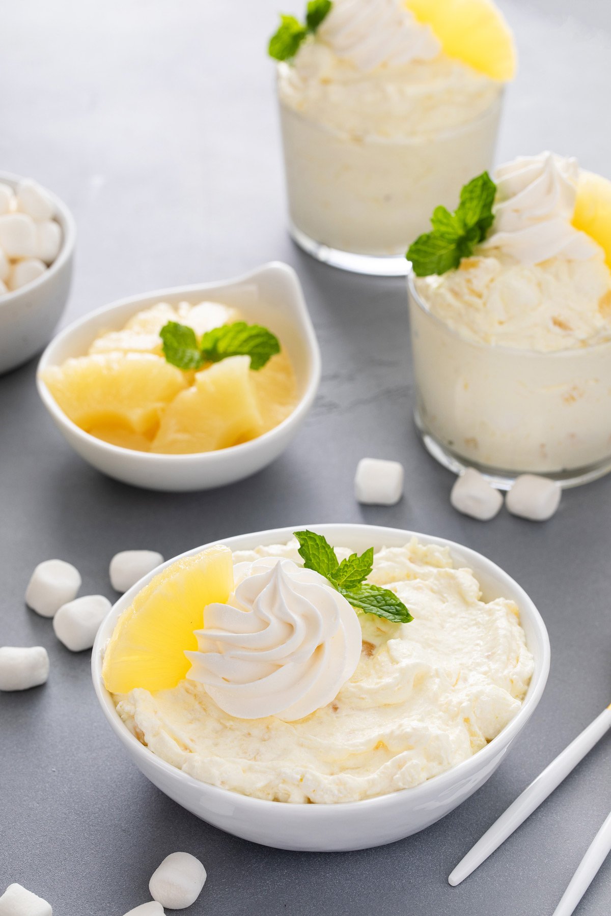 White bowl of pineapple fluff with two glass dishes of fluff in the background.