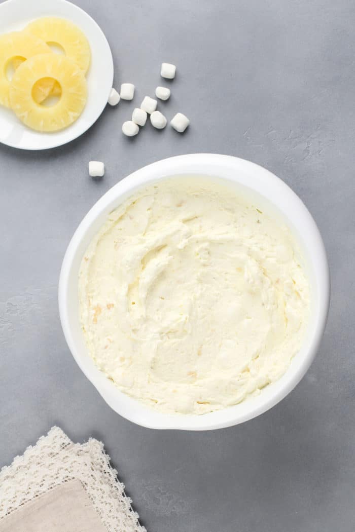 Pineapple fluff mixed together in a white mixing bowl, ready to be chilled in the fridge.