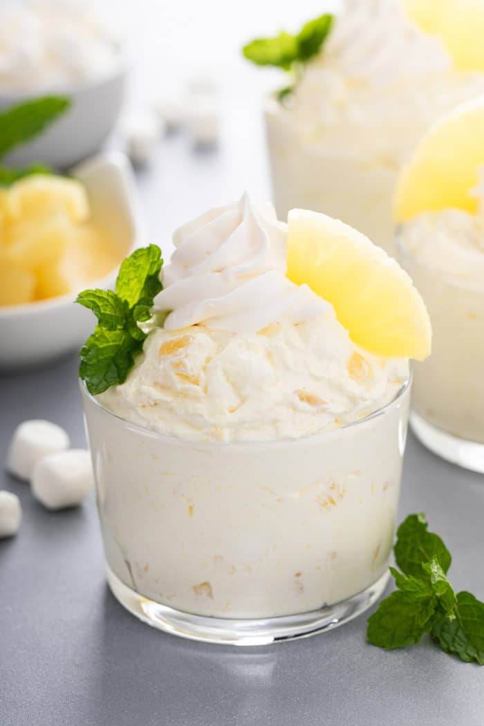 Closeup image of a glass cup filled with pineapple fluff and topped with whipped topping and pineapple.