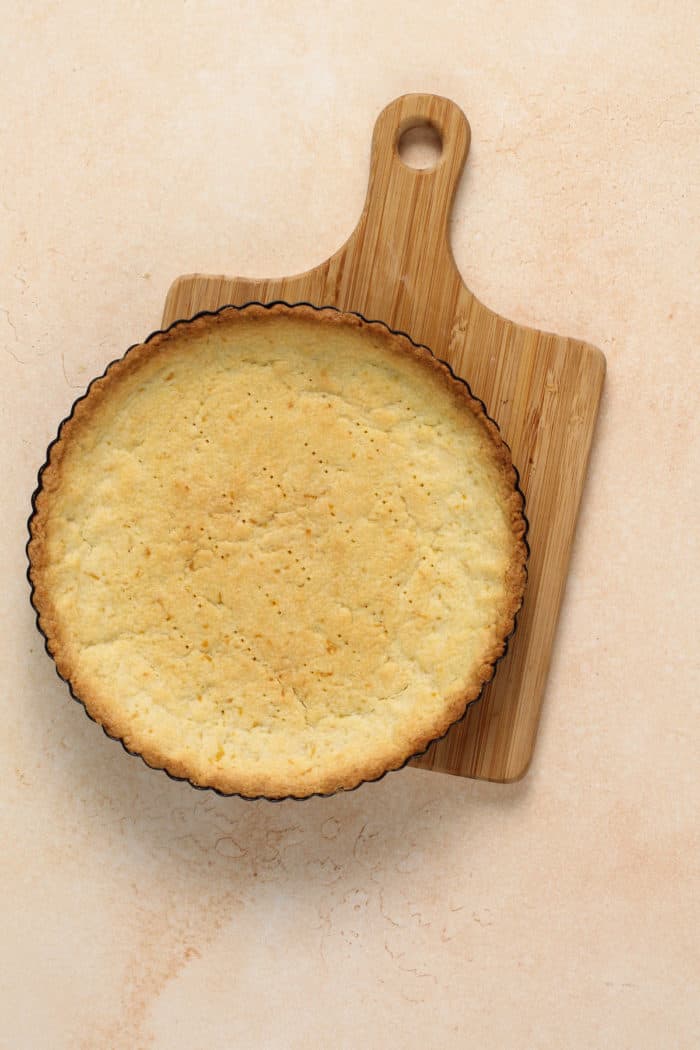 Baked tart shell cooling on a wooden board.