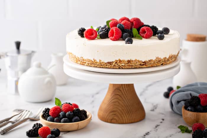 No-bake frozen cheesecake topped with mixed berries, set on a wooden cake stand