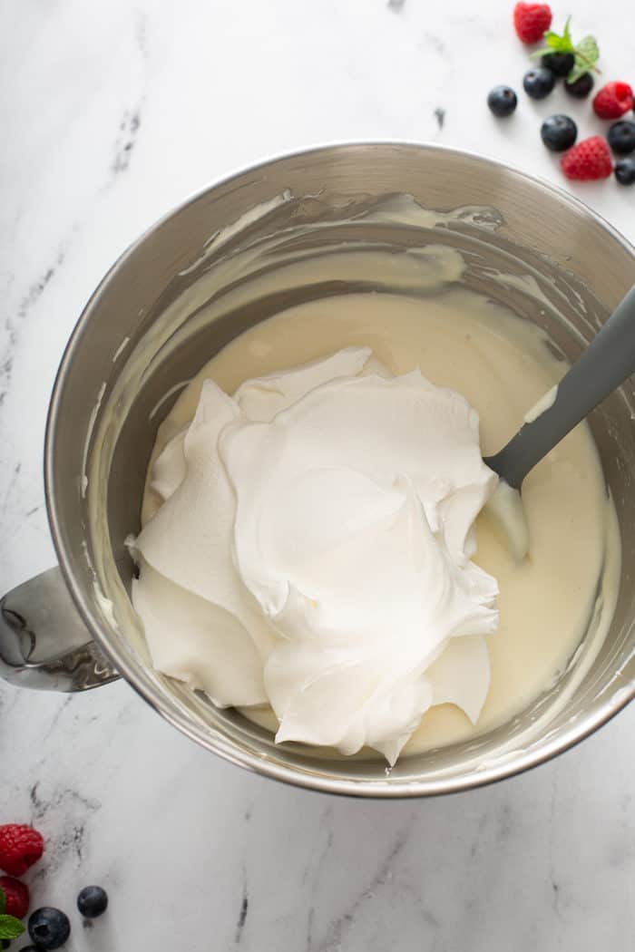 Spatula about to fold whipped topping into the filling for no-bake frozen cheesecake