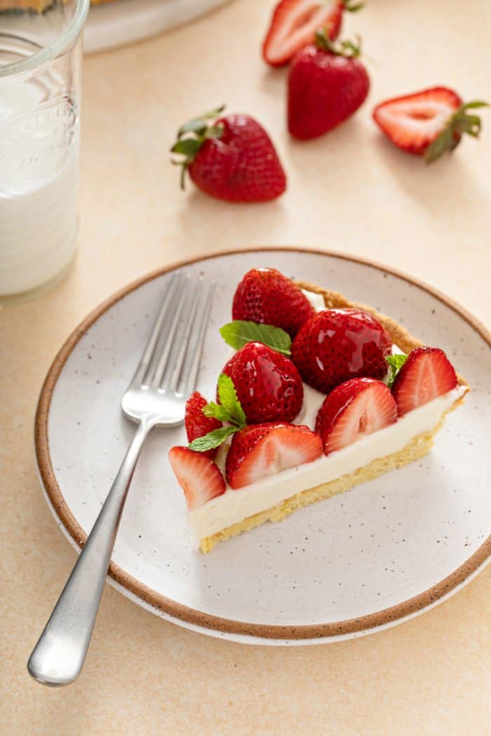 Slice of strawberry tart set next to a fork on a cream-colored plate.
