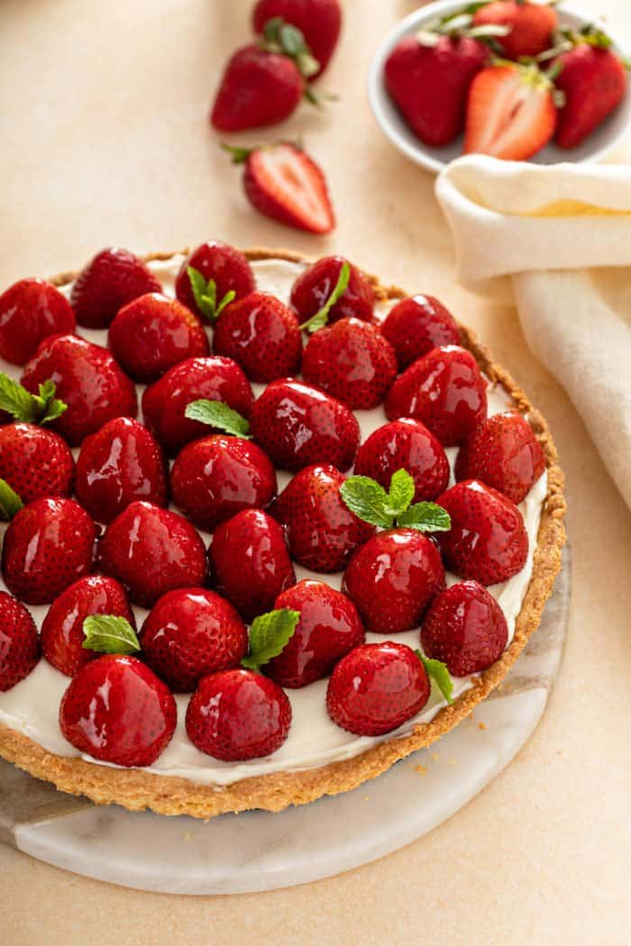 Whole strawberry tart set on a marble serving platter.
