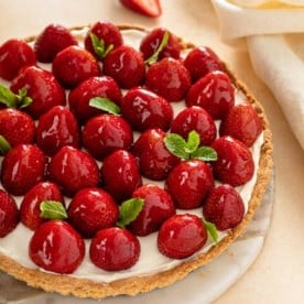 Tarte aux fraises, garnie de brins de menthe, servie dans un plat de service en marbre.