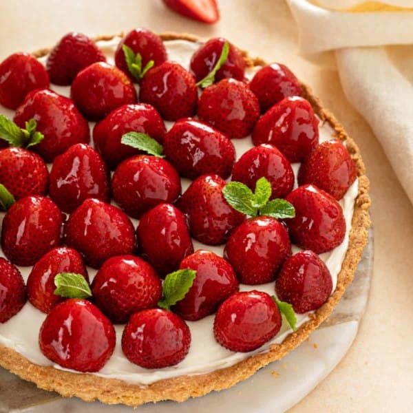 Strawberry tart, garnish with sprigs of mint, set on a marble serving platter.