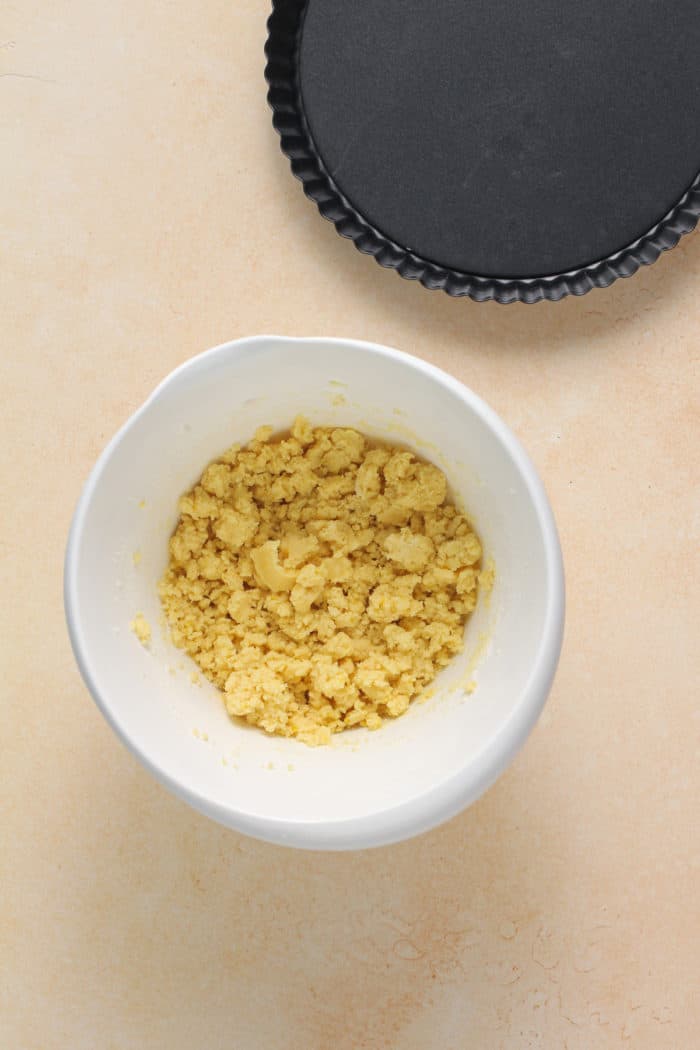 Tart crust dough in a white mixing bowl set next to a tart pan.