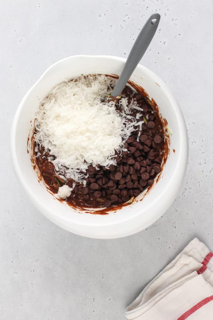 Shredded coconut and chocolate chips being added to chocolate zucchini bread batter.