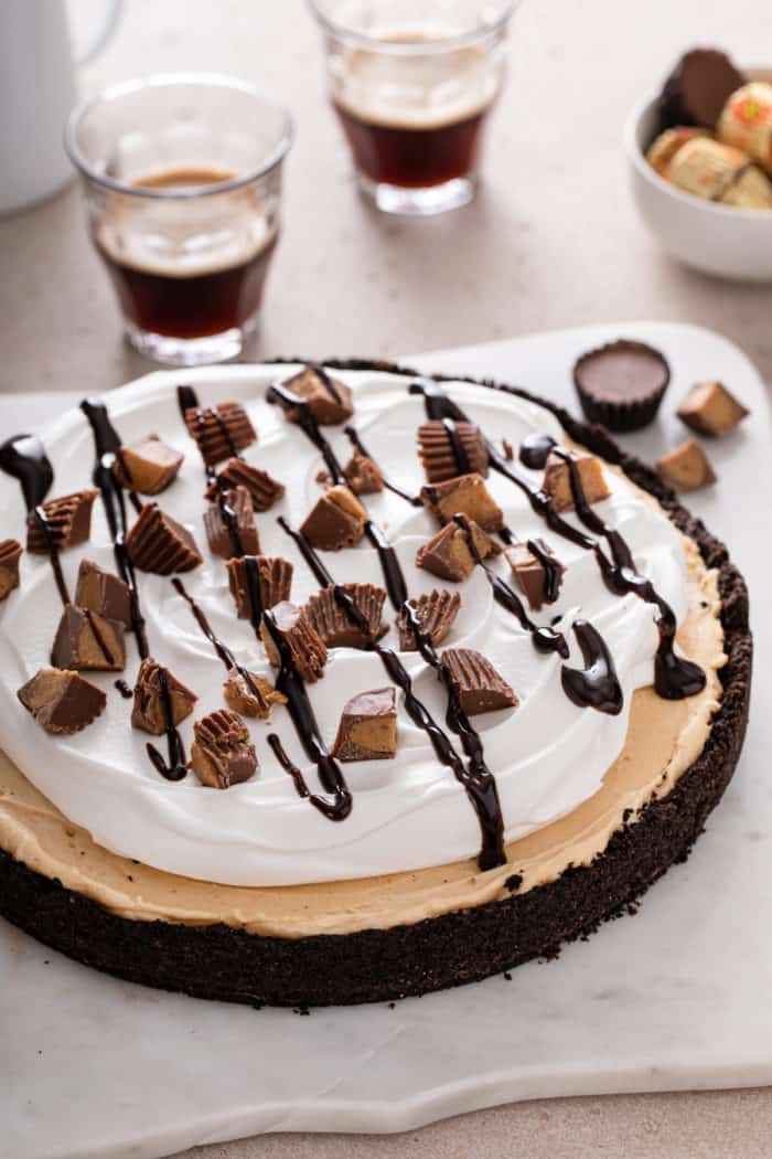 Peanut butter pie set on a slice of parchment paper and topped with chocolate sauce and chopped peanut butter cups.