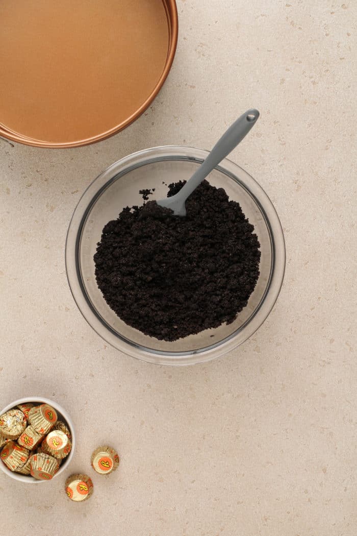 Oreo crumbs and melted butter stirred together in a glass mixing bowl.