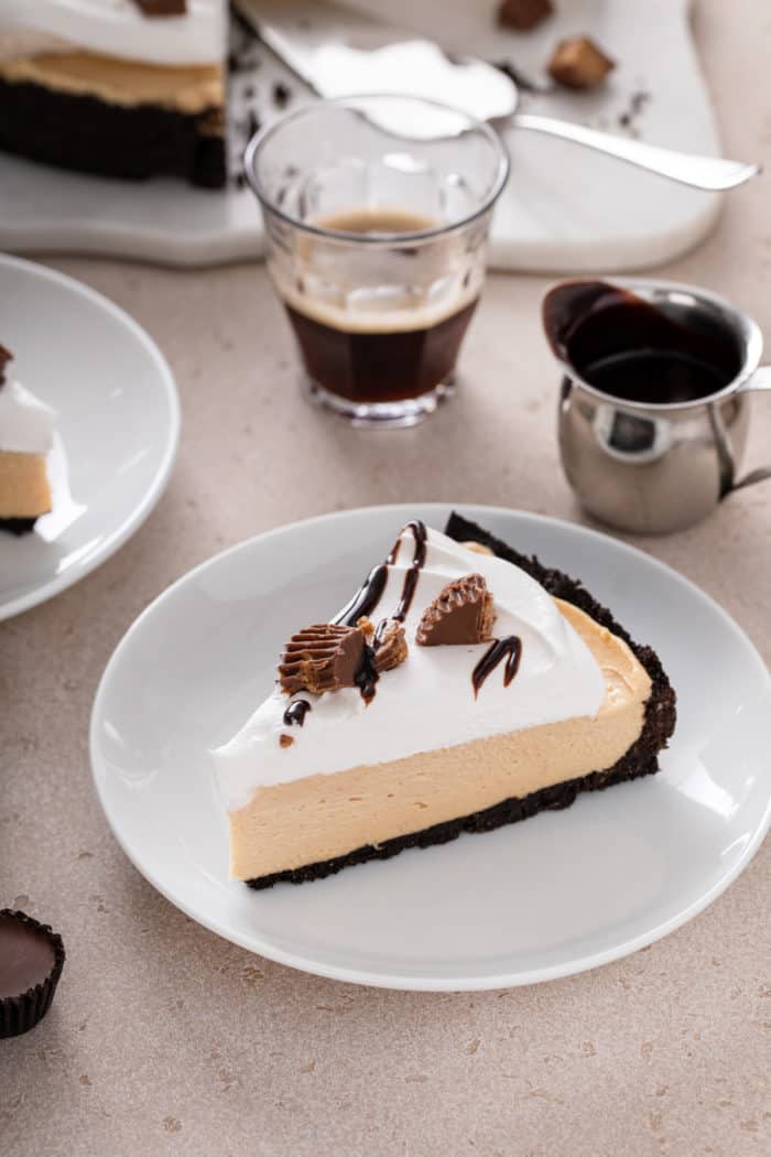 Slice of peanut butter pie topped with whipped cream, peanut butter cups, and chocolate sauce on a white plate.