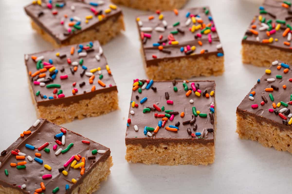 Cut scotcheroos arranged on a countertop. The bars are topped with rainbow sprinkles.