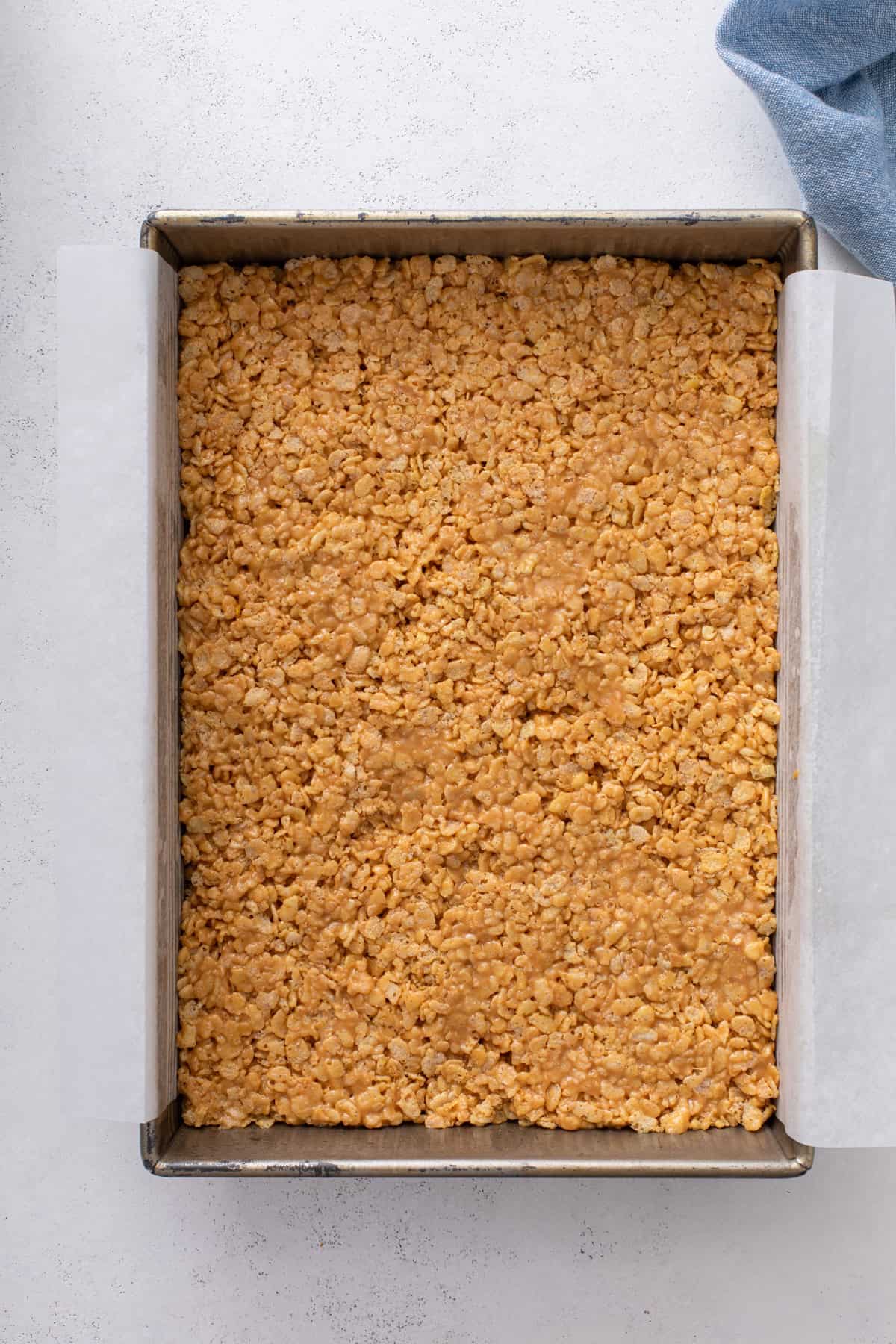 Cereal base for scotcheroos pressed into a parchment-lined pan.