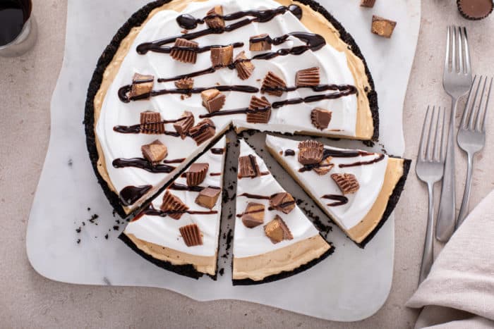 Overhead view of a sliced peanut butter pie, topped with whipped cream, peanut butter cups and chocolate sauce.