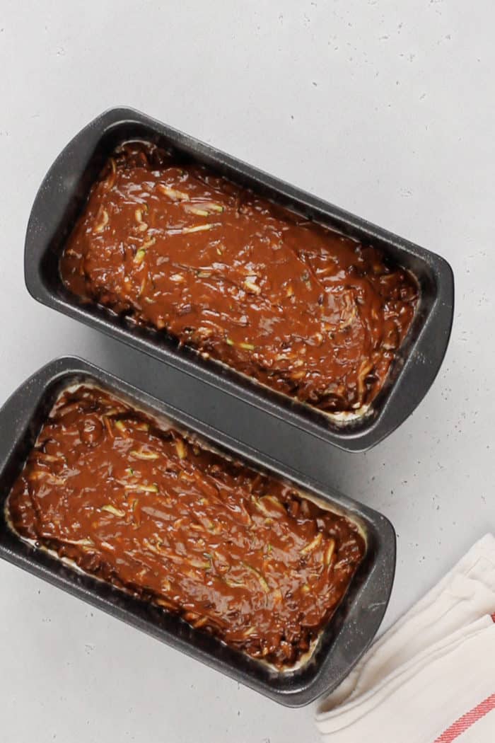 Chocolate zucchini bread batter in two loaf pans, ready to be baked.