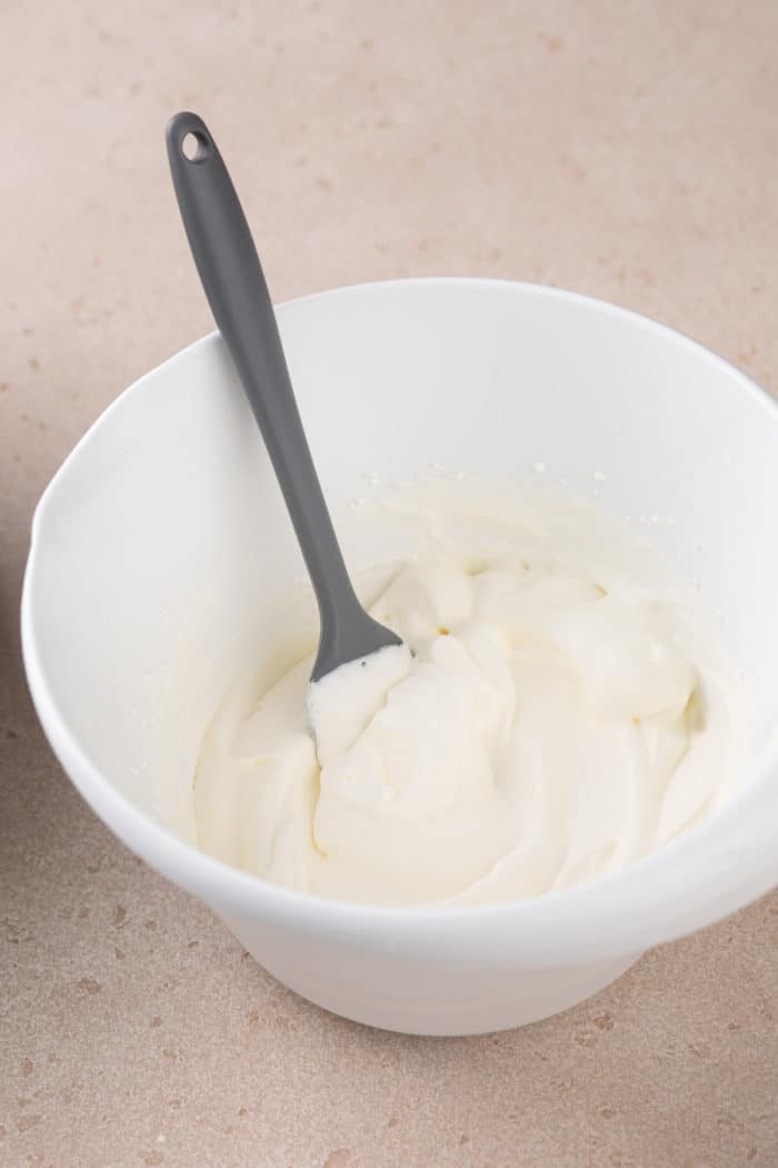 Whipped cream in a white mixing bowl with a gray spatula.