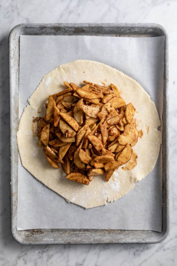 Apple galette filling on a circle of pie crust, set on a parchment-lined baking sheet.