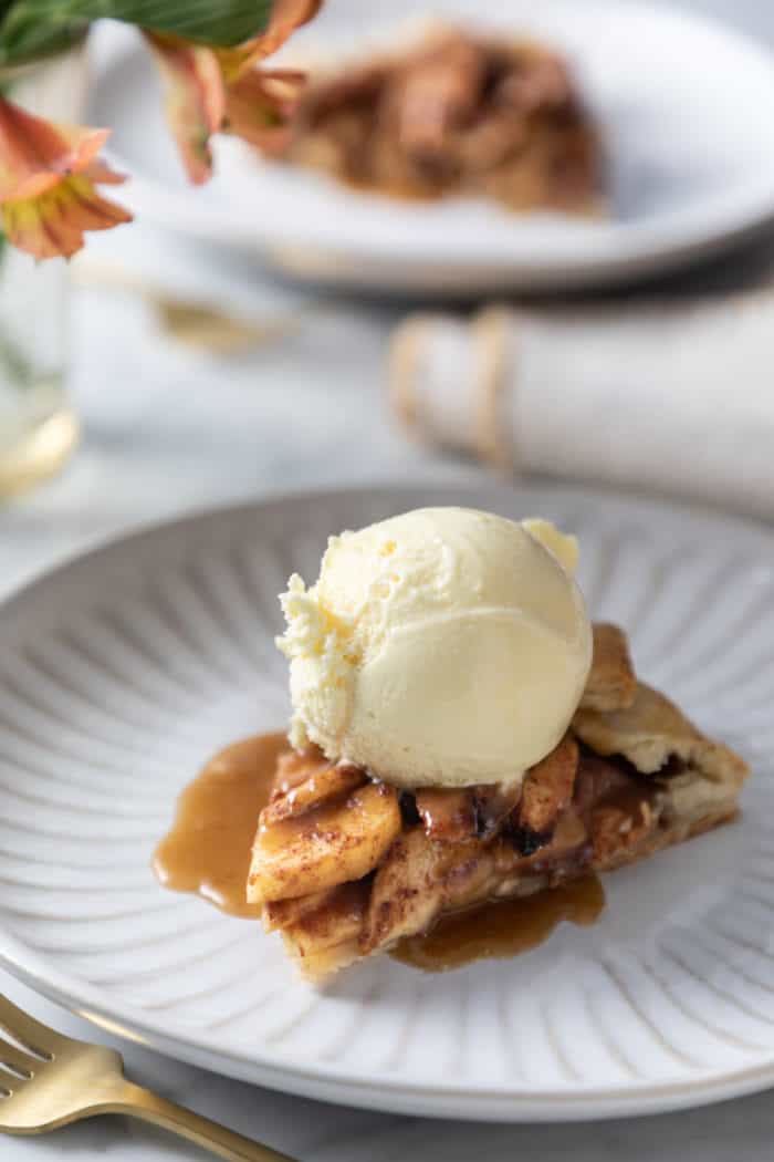 Scoop of vanilla ice cream on top of a sliced of plated apple galette.