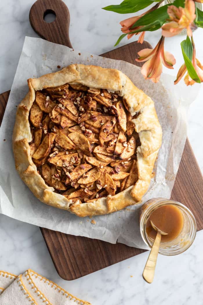 Baked apple galette set on a wooden cutting board next to a glass jar of salted maple glaze.