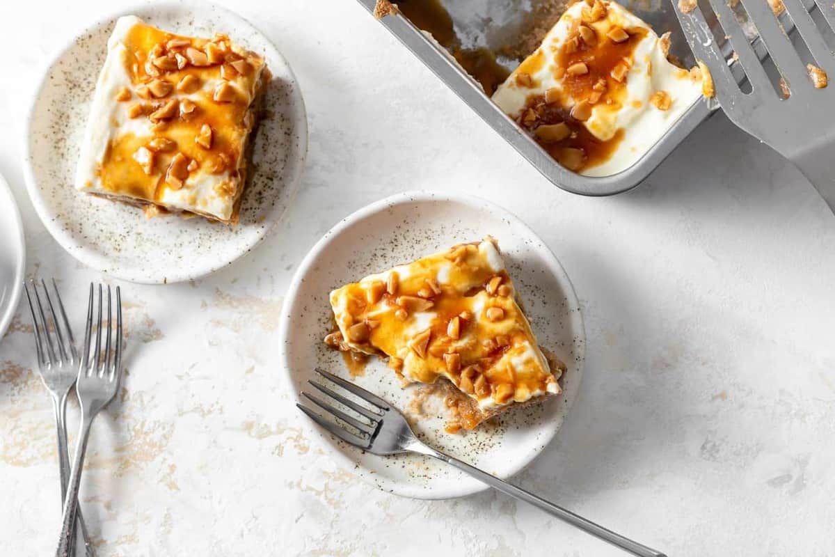 Caramel apple poke cake topped with whipped topping and toffee bits, on a plate with several bites taken out of it