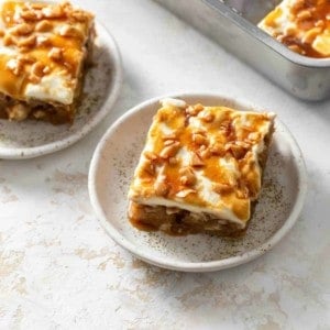 Plated slices of caramel apple poke cake, with full cake in the background