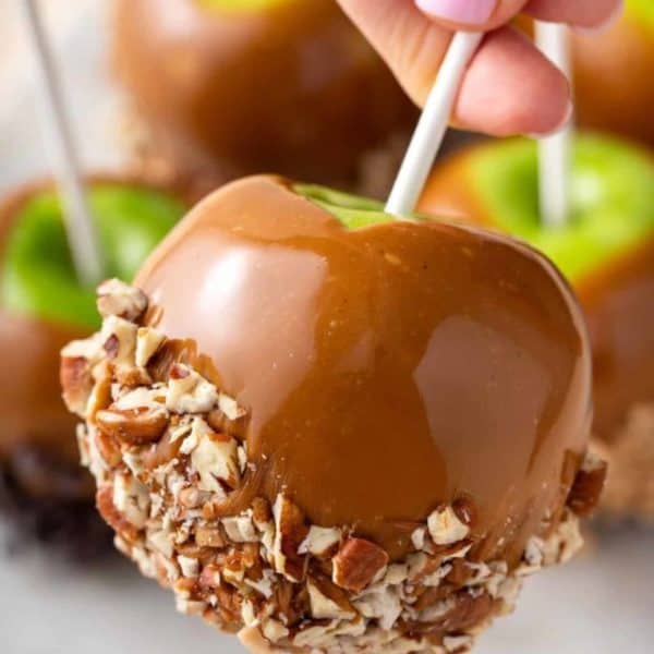 Hand holding up a caramel apple dipped in chopped pecans.