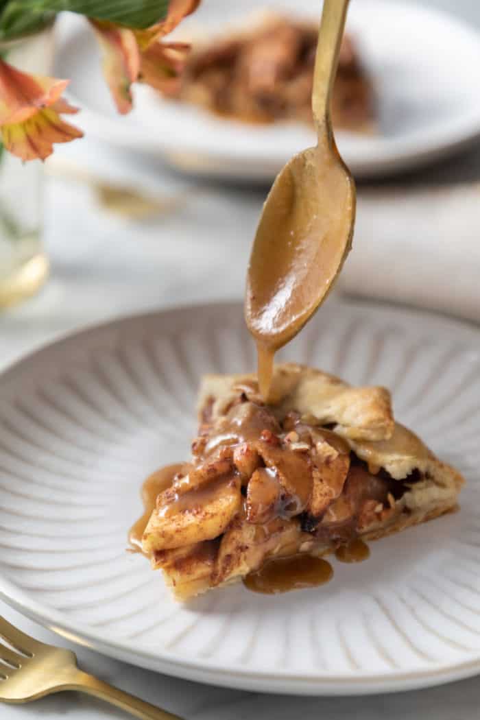 Spoon drizzling salted maple glaze over a slice of apple galette.