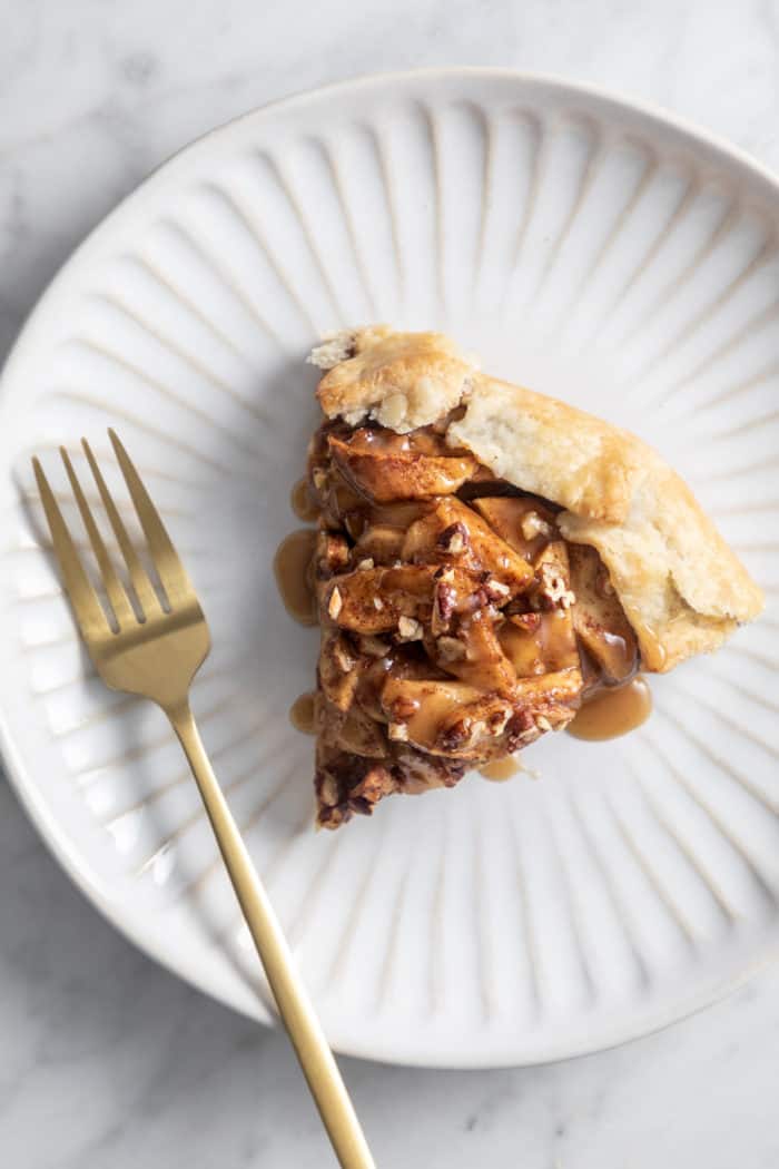 Overhead view of slice of apple galette topped with maple glaze on a white plate.