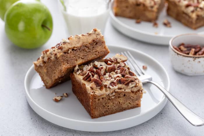 Two caramel apple blondies next to a fork on a white plate.