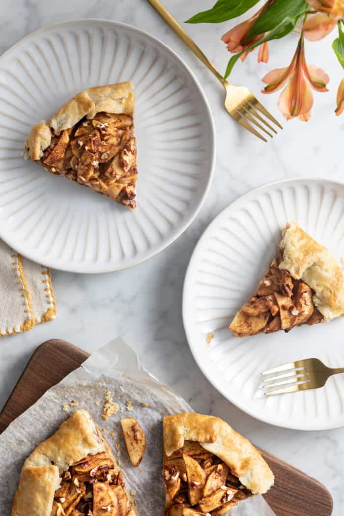 Two white plates, each with a slice of apple galette, set next to a wooden cutting board with sliced galette.