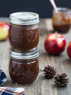 Two small jars of apple butter stacked on top of each other on a wood table