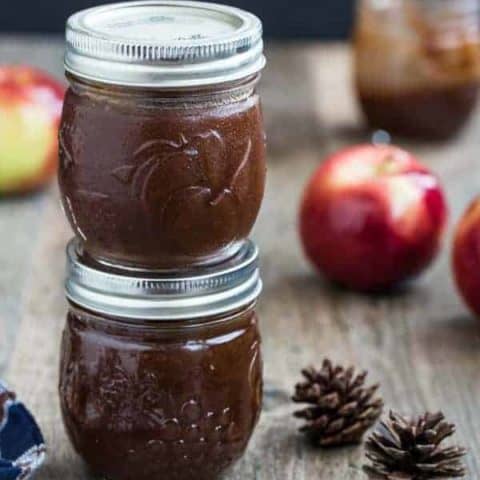 Two small jars of apple butter stacked on top of each other on a wood table