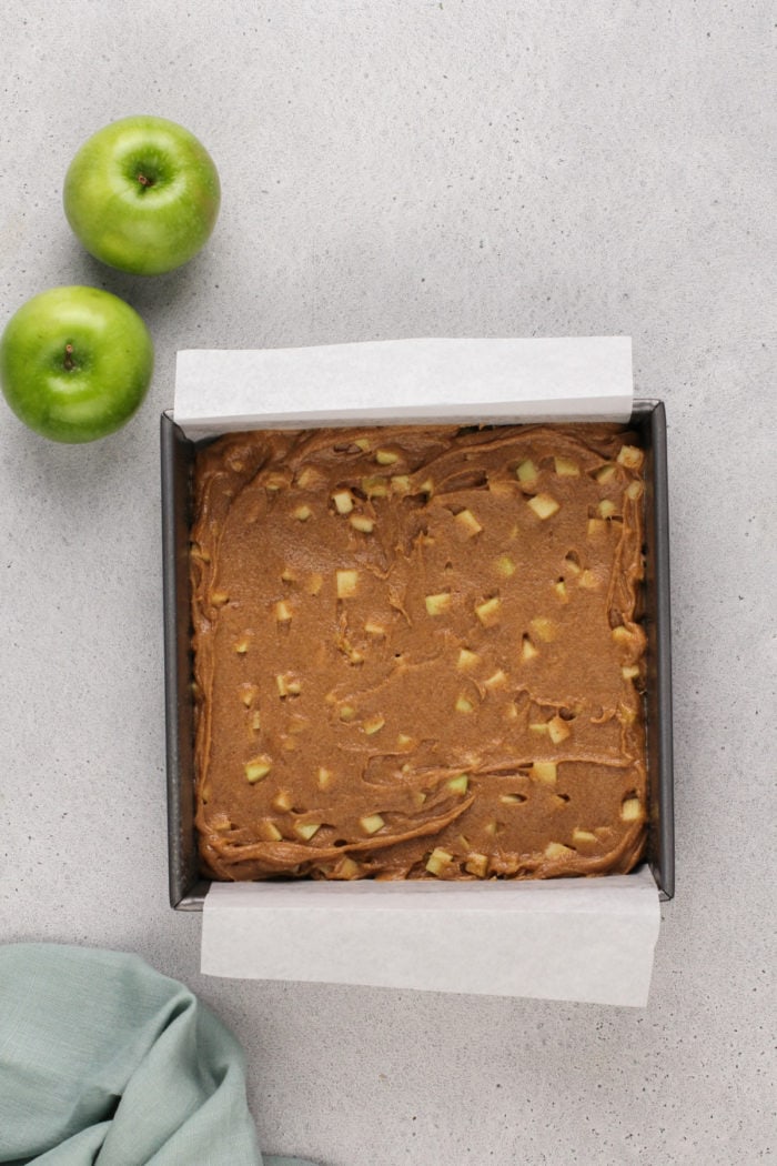 Caramel apple blondie batter in a parchment-lined pan, ready to go in the oven.