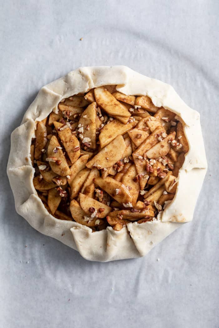 Unbaked apple galette on a piece of parchment paper.