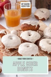 Glazed apple cider donuts cooling on a wire rack. A glass of cider and whole apples are in the background. text overlay includes recipe name.