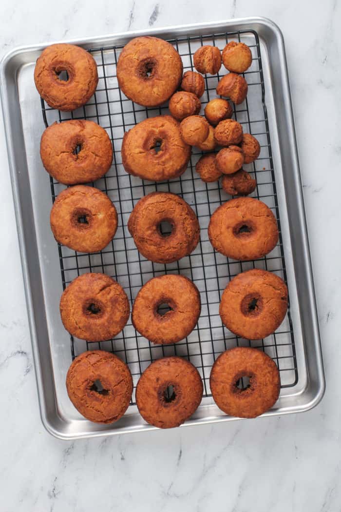 Fried apple cider donuts cooling on a wire rack.