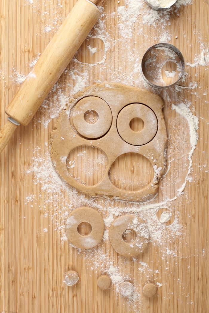 Apple cider donuts being cut from rolled out dough on a wooden surface.