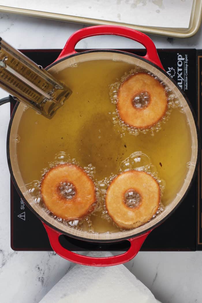 Three apple cider donuts frying in a dutch oven.