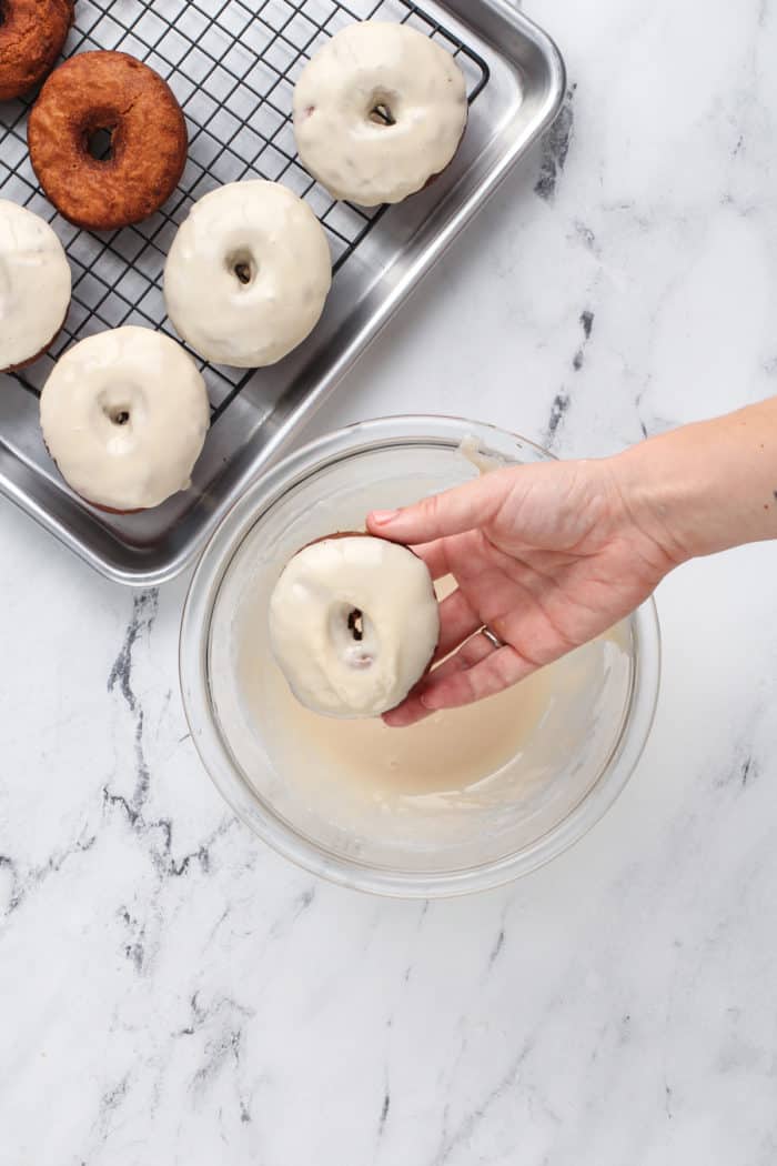 Apple cider donut being dipped into cider glaze.