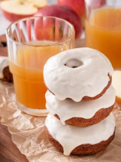 Three stacked apple cider donuts next to a glass of cider.