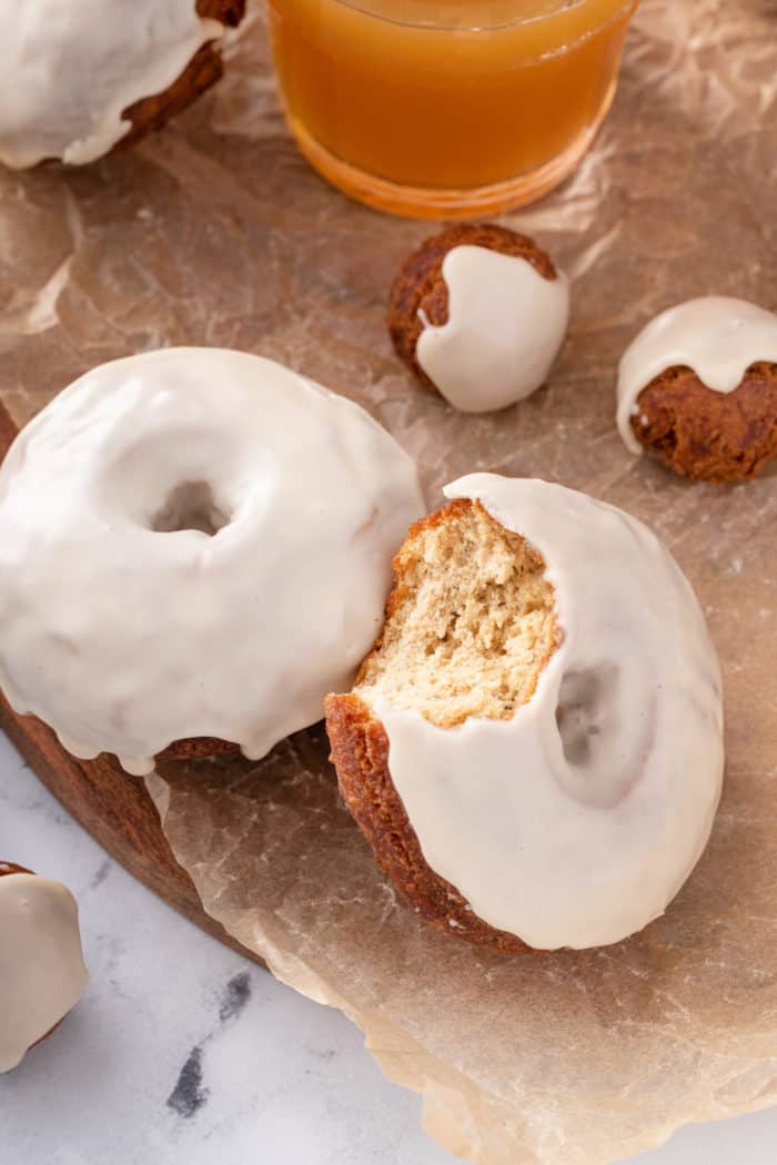 Two apple cider donuts on a piece of parchment paper. A bite has been taken from one of them.