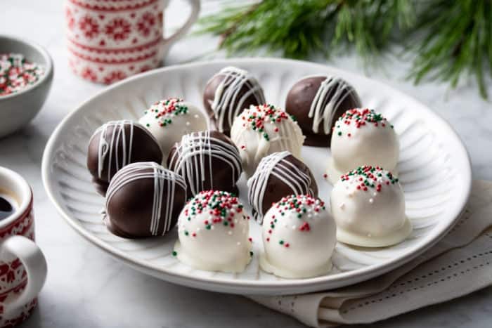 White plate filled with chocolate-covered peanut butter balls decorated with red and green sprinkles.